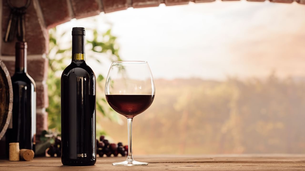 glass and bottle of wine sit next to a barrel in front of a landscape vista