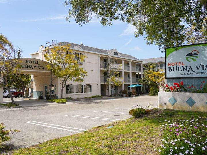 A three-story hotel building with balconies and a parking lot.