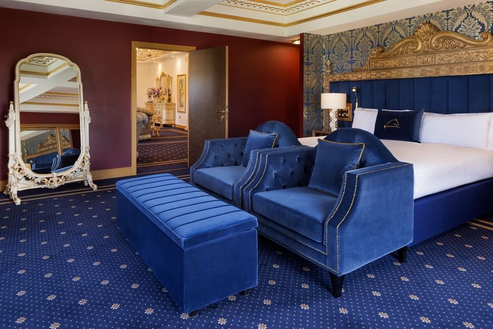 King bed and blutufted armchairs with a velvet ottoman beside a vintage standing mirror in a suite at Polo Club Hotel