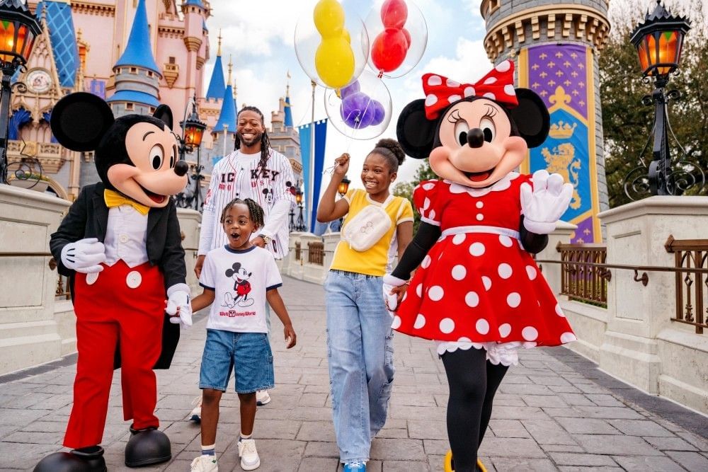 A boy, girl, and their father walk hand in hand with Mickey and Minnie Mouse in front of Cinderella Castle, smiling and carrying balloons.