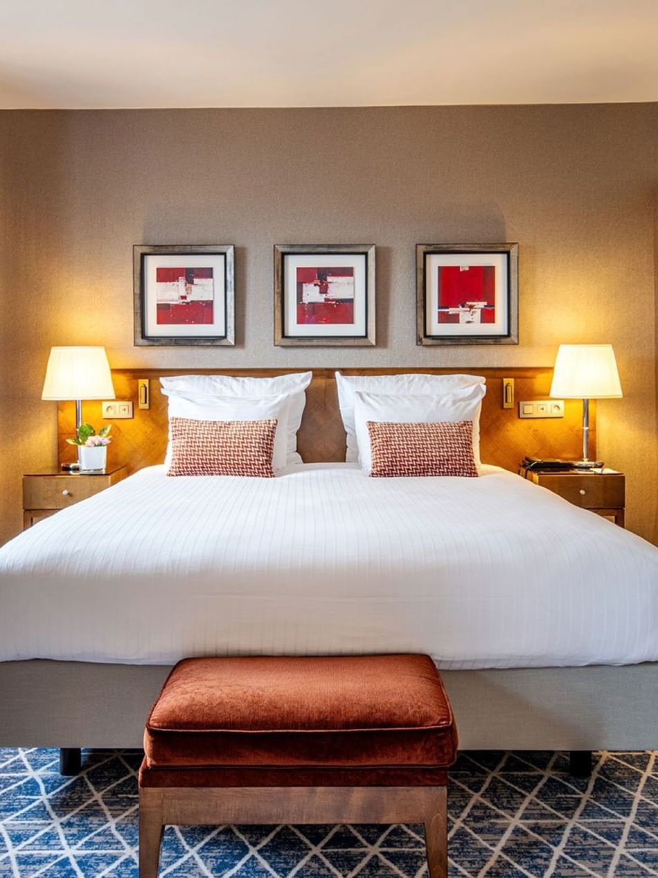 Bed between side tables with ottoman beside wooden cabinet in Warwick Suite at Warwick Grand Place Brussels