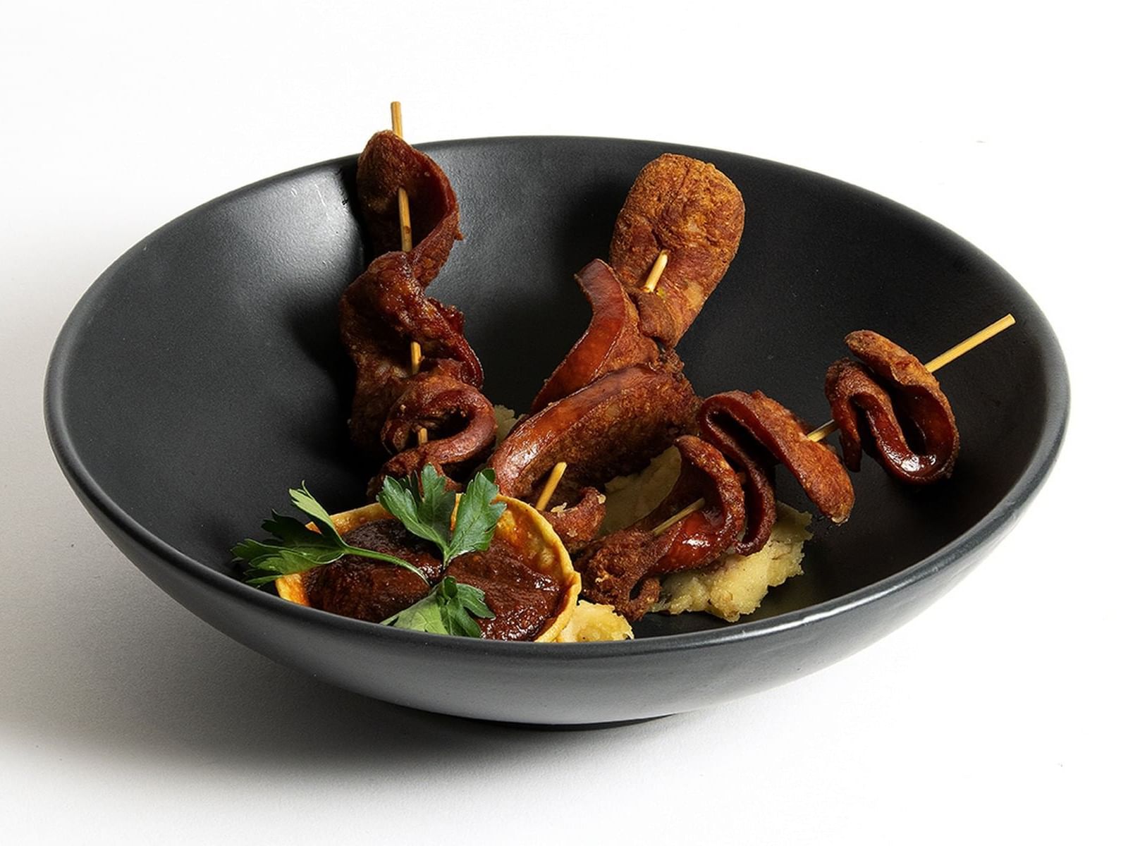 Grilled chicken feet skewers in a black bowl with mashed potatoes and parsley at Live Aqua San Miguel de Allende