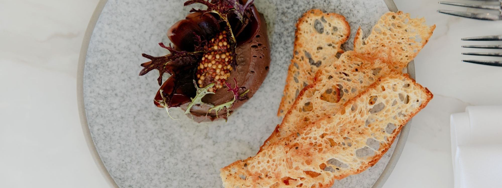 Plate with chocolate mousse, garnish, and crispy bread slices, set on a table with cutlery and napkins.