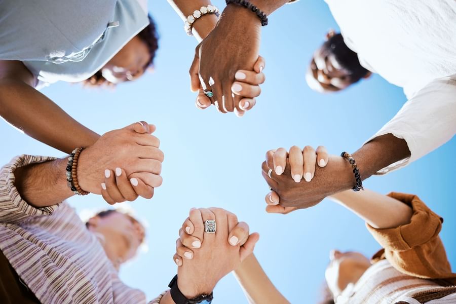 Diverse group holding hands in circle under blue sky near Warwick Corporate