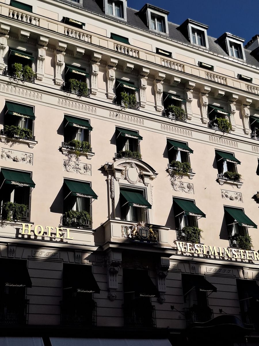 Exterior facade with green awnings and lush plants at Hotel Westminster Paris, featuring gold signage by the stone wall