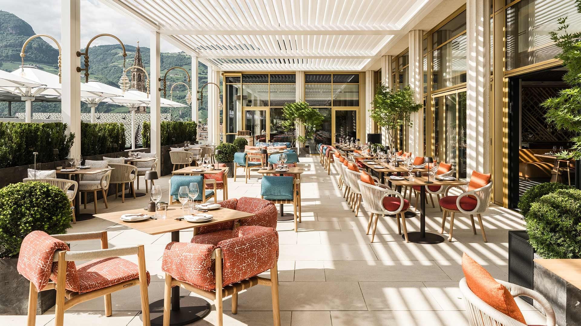 Ristorante all'aperto con tavoli e sedie, piante e vista su una montagna.