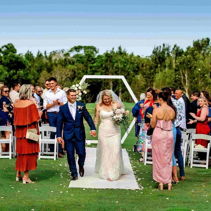 Outdoor wedding ceremony with guests and the couple on the aisle at Mercure Kooindah Waters