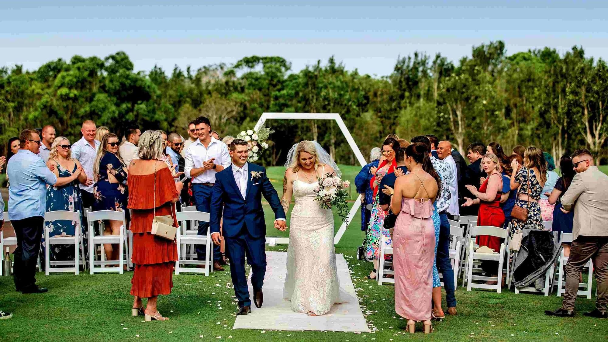 Outdoor wedding ceremony with guests and the couple on the aisle at Mercure Kooindah Waters