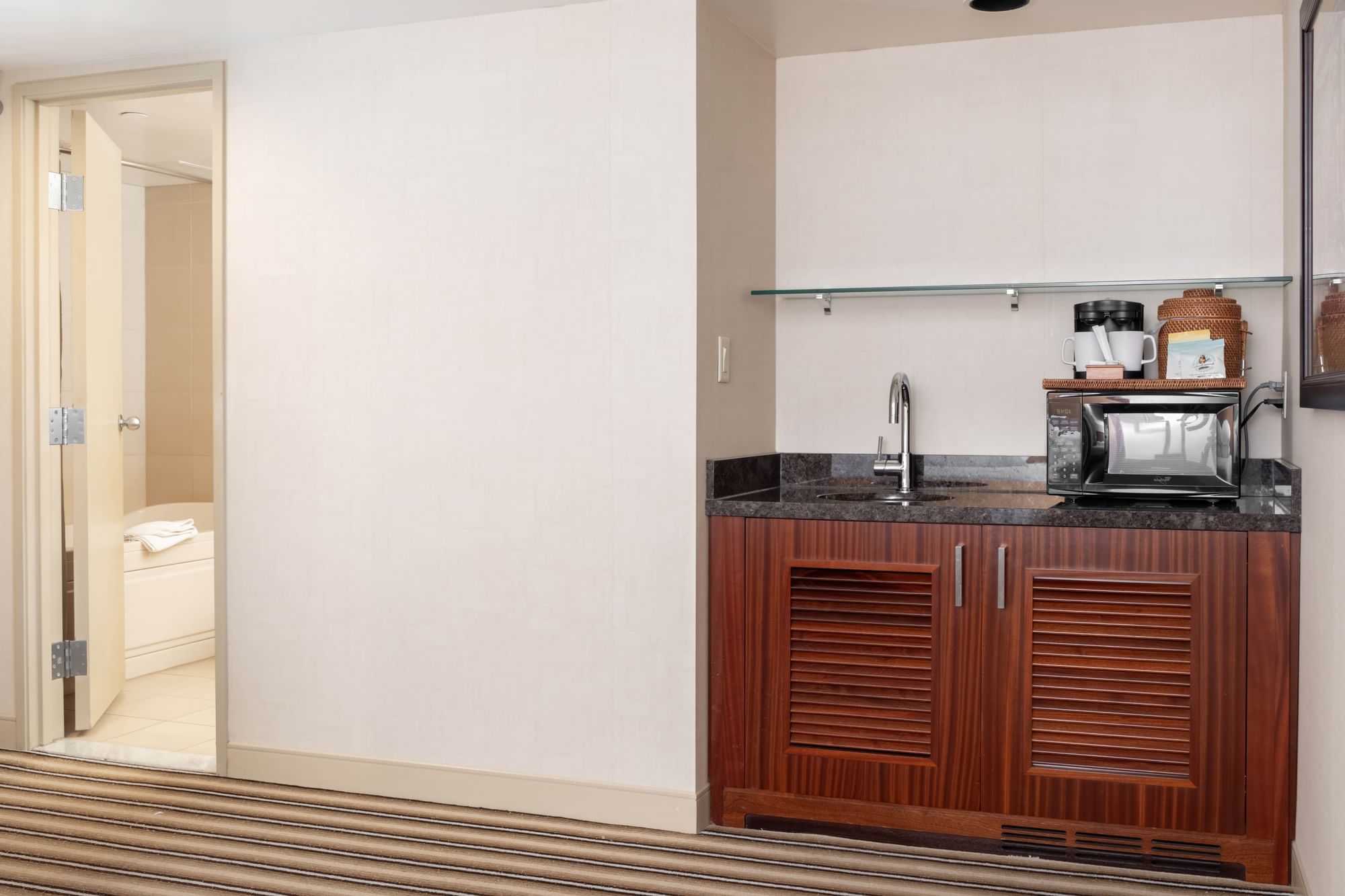 A hotel room kitchenette with a microwave, coffee maker, and sink.
