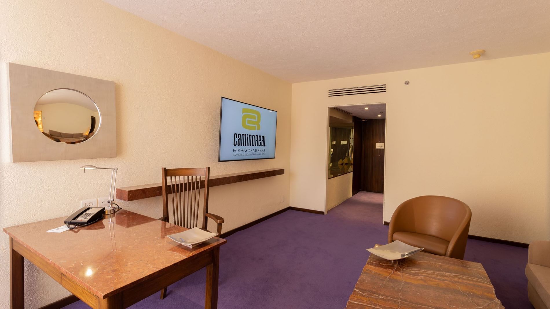 Sala de recepción de hotel con mesa, sillas, televisión y alfombra púrpura.