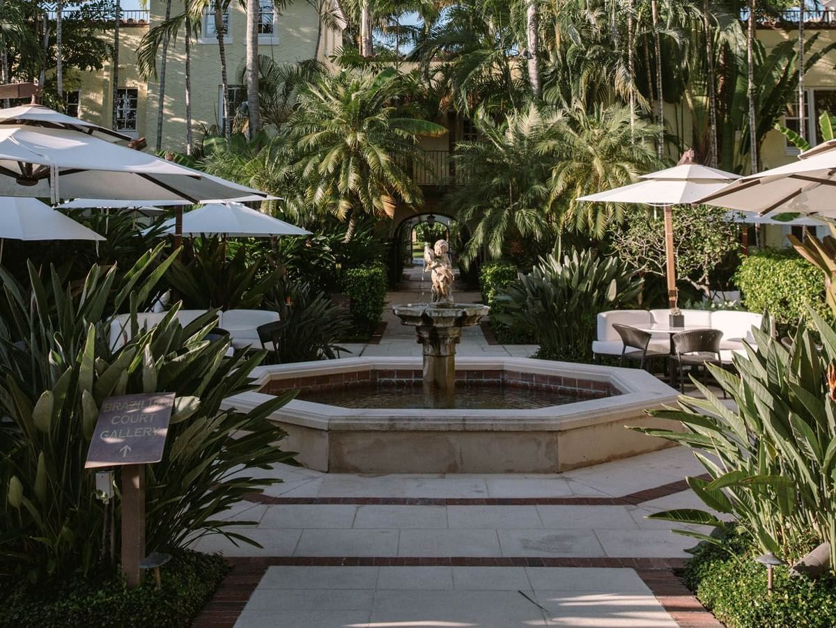 Tiered stone fountain surrounded by white umbrellas and palm trees in the courtyard at The Brazilian Court