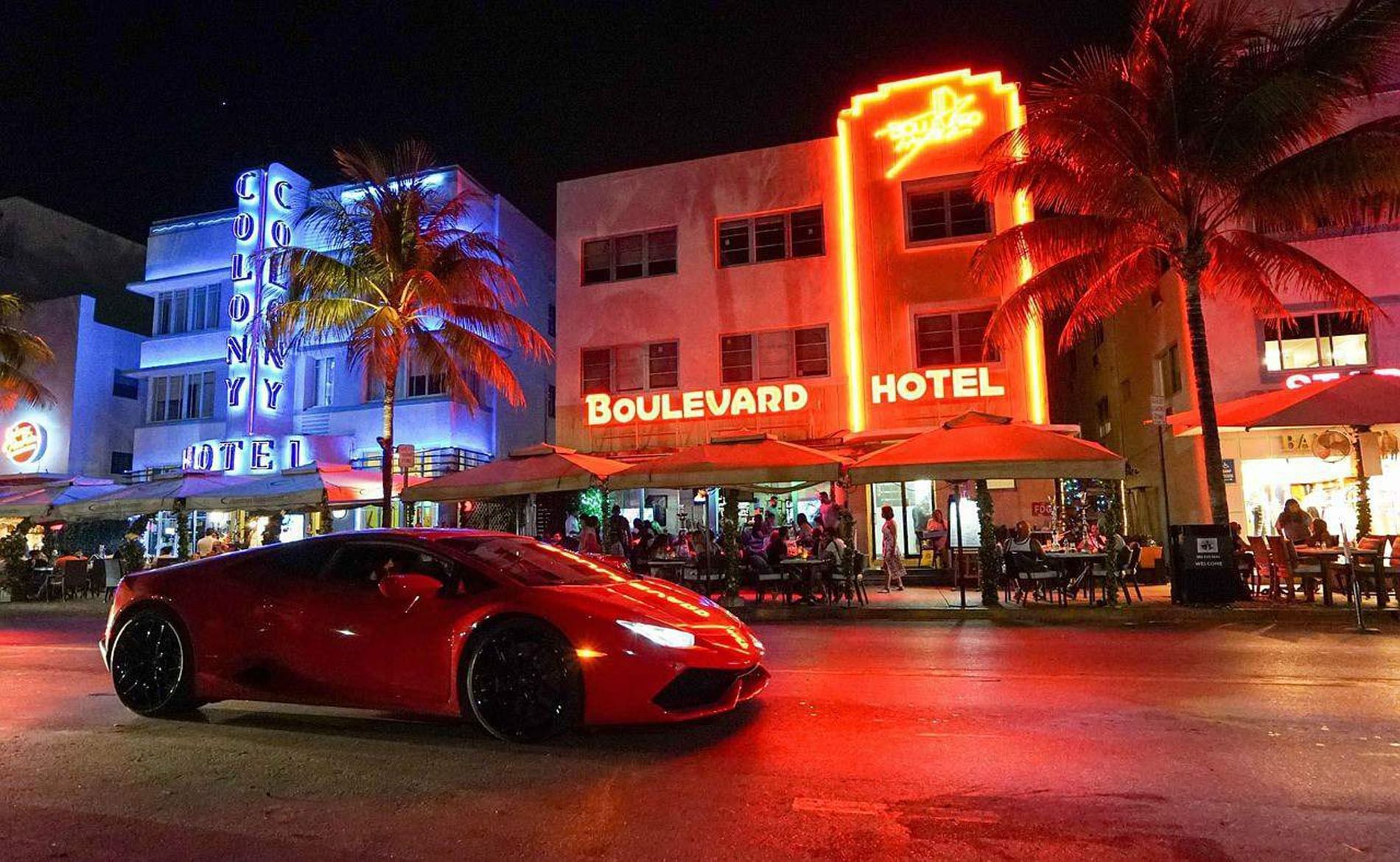 A nighttime exterior view of a hotel with a red sports car in front of it.