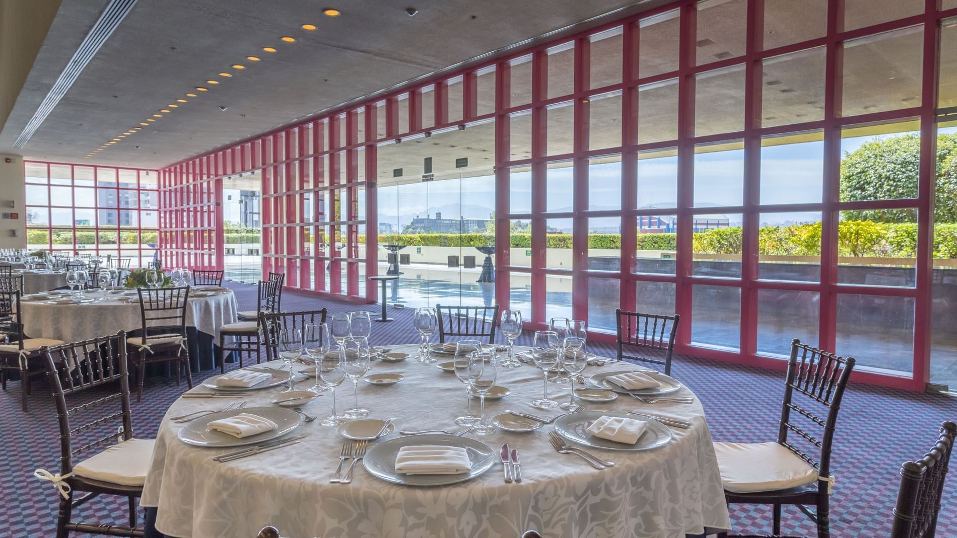 Event room with round tables near windows and a bright red grid frame at Camino Real Polanco Mexico
