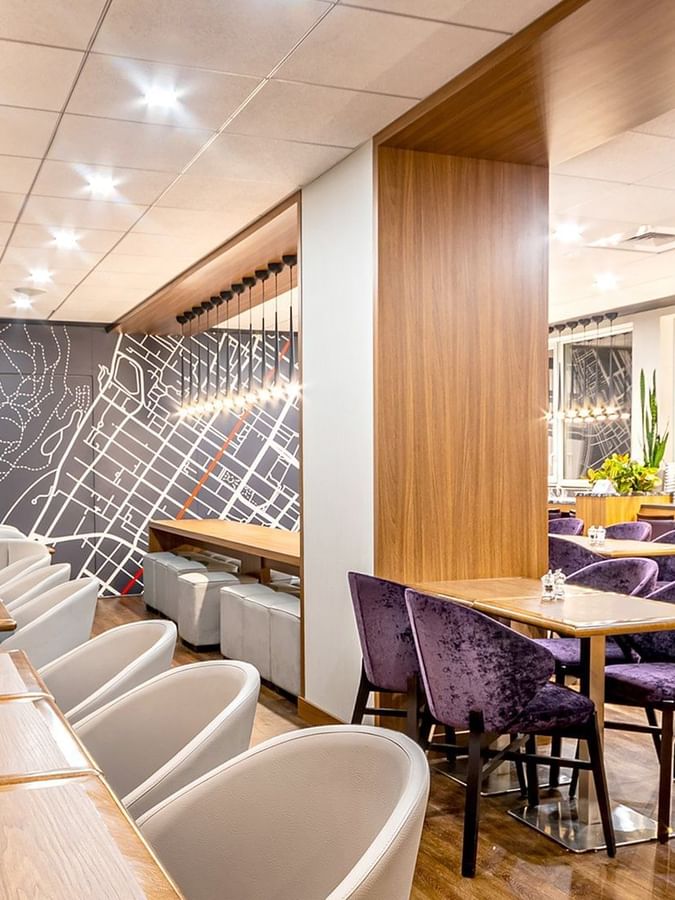 Purple velvet chairs by wooden tables near a decorative map wall in Espace Ste. Catherine at Warwick Le Crystal Montreal