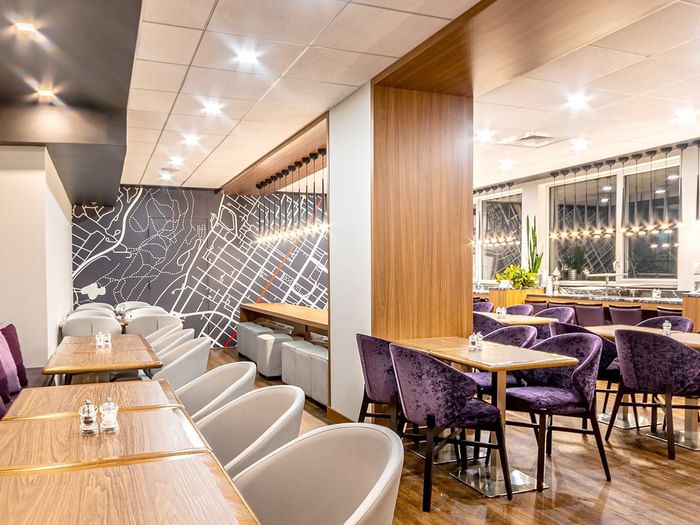 Purple velvet chairs by wooden tables near a decorative map wall in Espace Ste. Catherine at Warwick Le Crystal Montreal