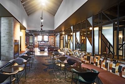 Spacious lounge area with modern decor, round tables with chairs, and a gallery wall at Amora Herencia Riverwalk Melbourne