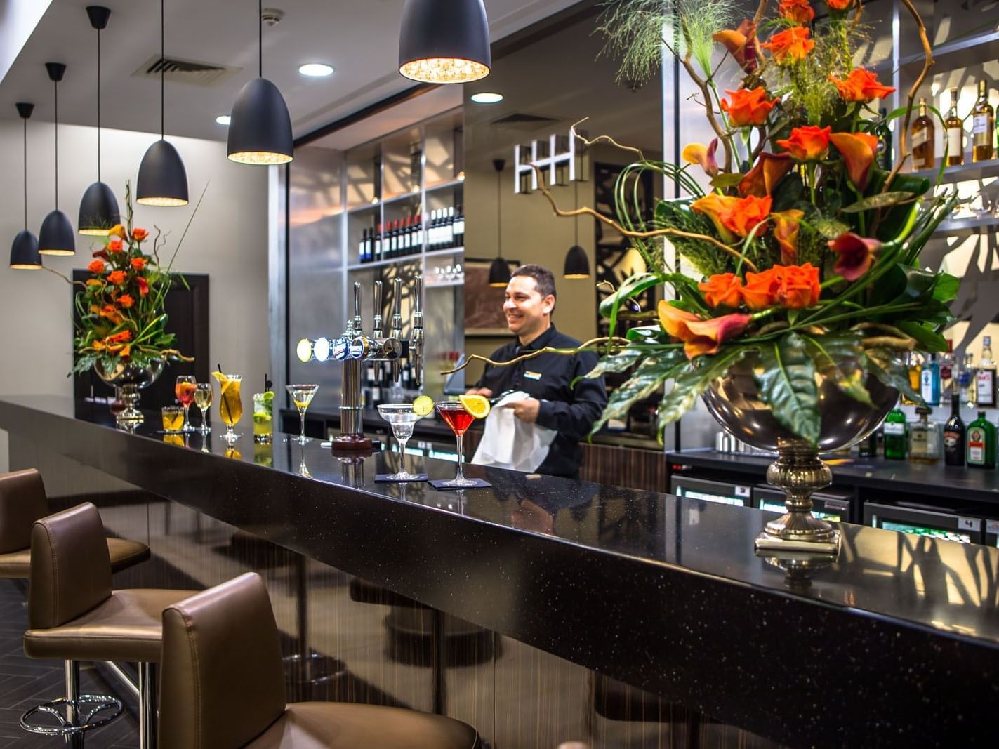 Atrium Bar with vibrant floral displays, cocktails on the counter, and a bartender preparing drinks at Heston Hyde Hotel