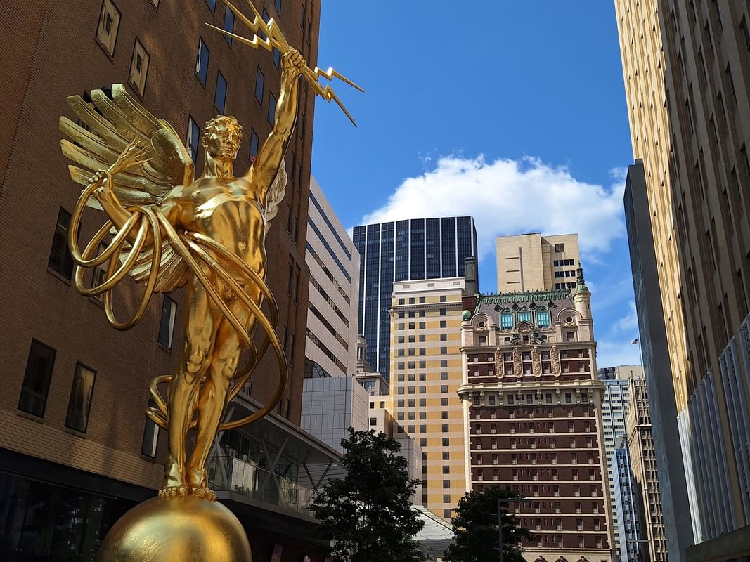 Golden winged statue by tall buildings under a blue sky near Warwick Melrose Dallas