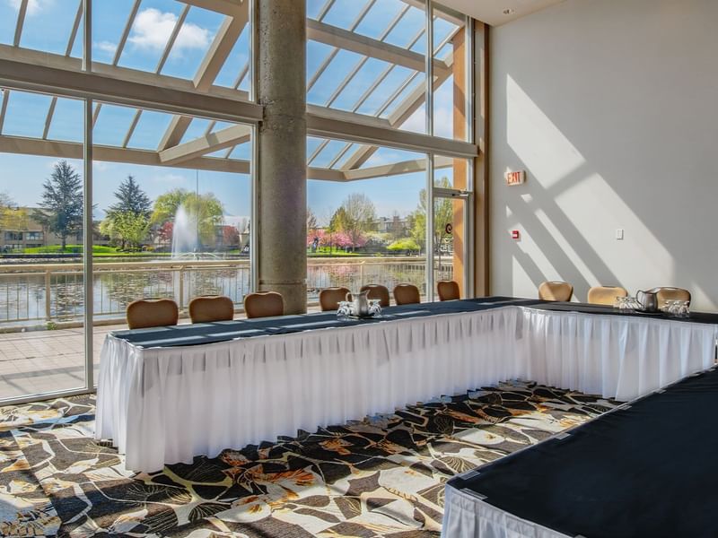Indoor conference room with long tables, chairs, and a view of a pond.