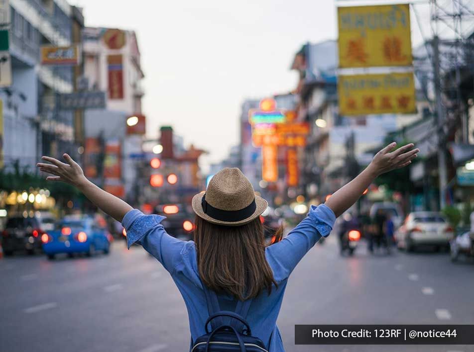 Traveler with arms outstretched in the middle of a lively city street - Lexis Port Dickson