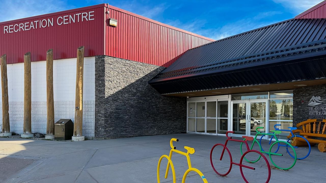 Modern recreation center with red metal siding, stone accents, and colorful bicycle sculptures at the entrance.