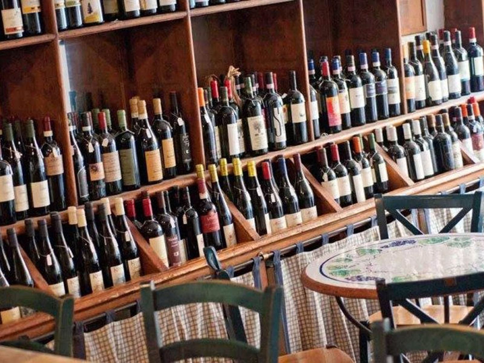 Wooden shelf filled with various wine bottles, alongside a round tables in Al Vino Al Vino near The Glam Hotel