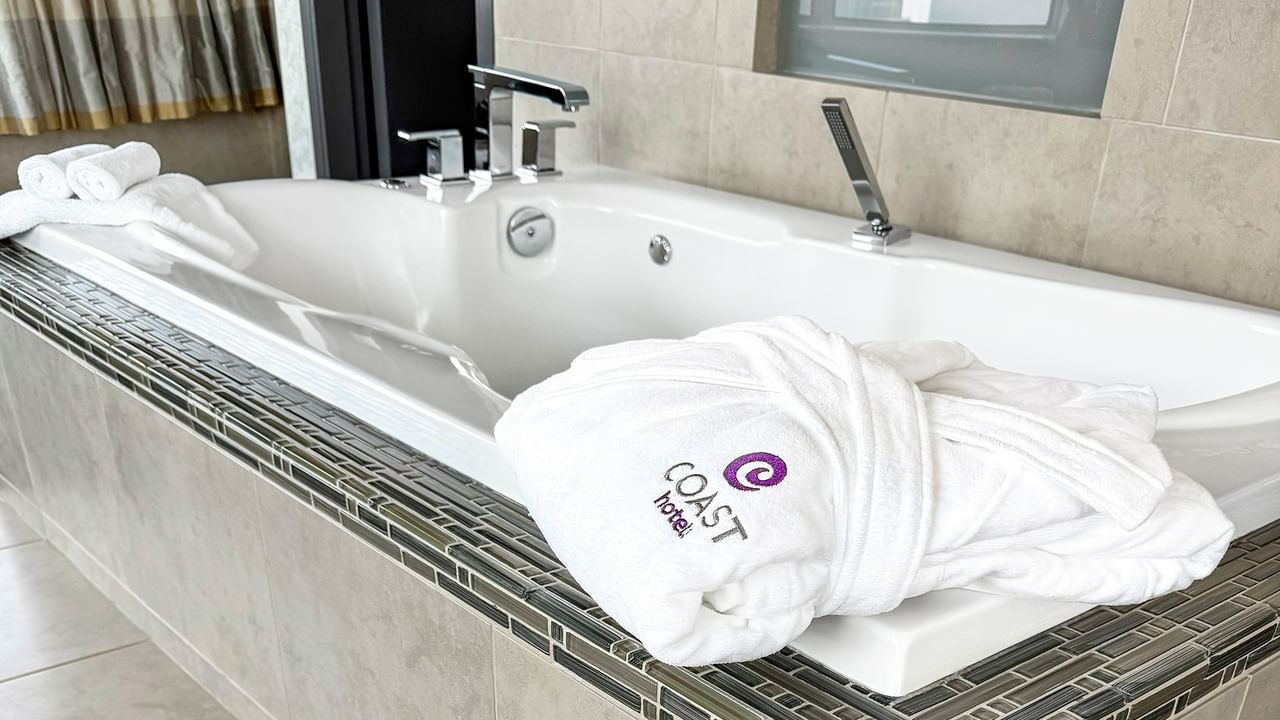 Coast Carrie Cates Penthouse Suite bathtub and a white robe at Coast Lonsdale Quay Hotel