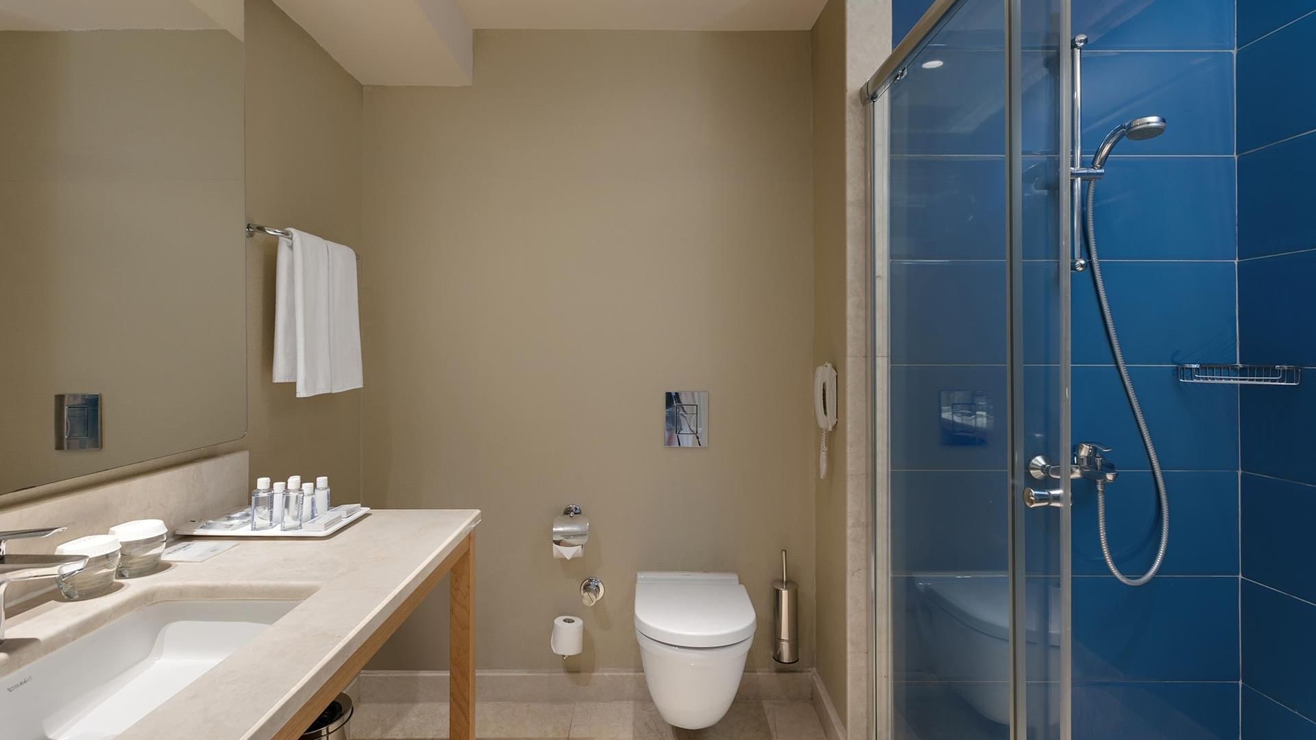 Titanic Deluxe Lara – Annex Standard Pool’da mavi fayanslı, duşakabinli ve aynalı modern bir banyo.