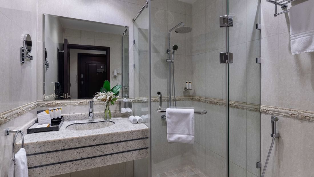 Granite sink with toiletries by a glass shower cubicle and a large mirror in Standard Room at Warwick Al Jubail