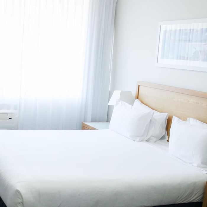 Art hung on a wall by a bed arranged with plush white pillows in a Hotel Room at Mercure Charlestown