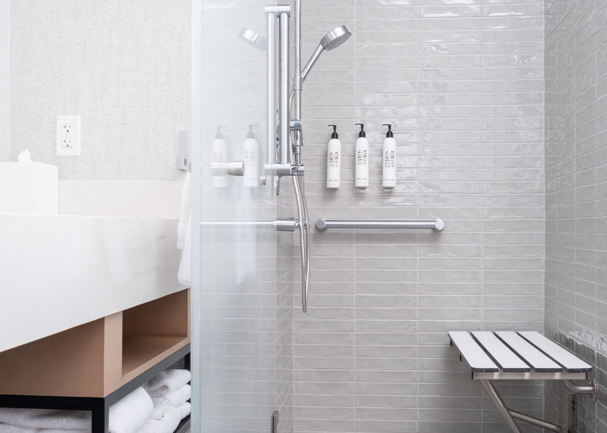 A bathroom shower with a glass door, silver shower head, and white tiles.