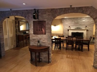 Wooden dining table by dark chairs, under a brick archway near a stone fireplace and wall mirror at Simsbury 1820 House