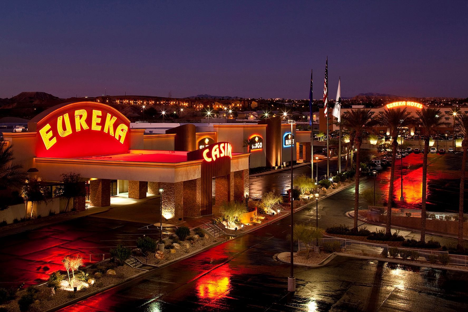 Aerial view of Eureka Casino Resort illuminated at night, with palm-lined roads and glowing casino signs near The Brook