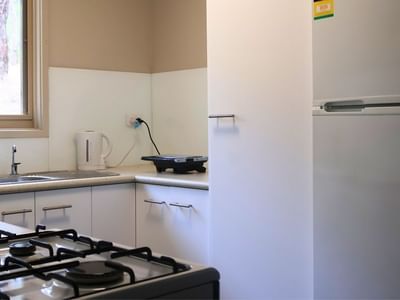 Modern kitchen with gas stove, sink, white cabinets, and refrigerator at La Trobe University Villas.