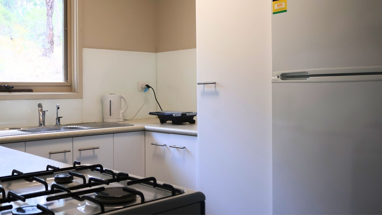 Modern kitchen with gas stove, sink, white cabinets, and refrigerator at La Trobe University Villas.