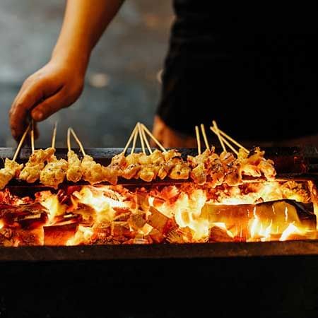 Close-up of a person grilling meat skewers on the BBQ, Malaysian street food tour near Imperial Lexis Kuala Lumpur