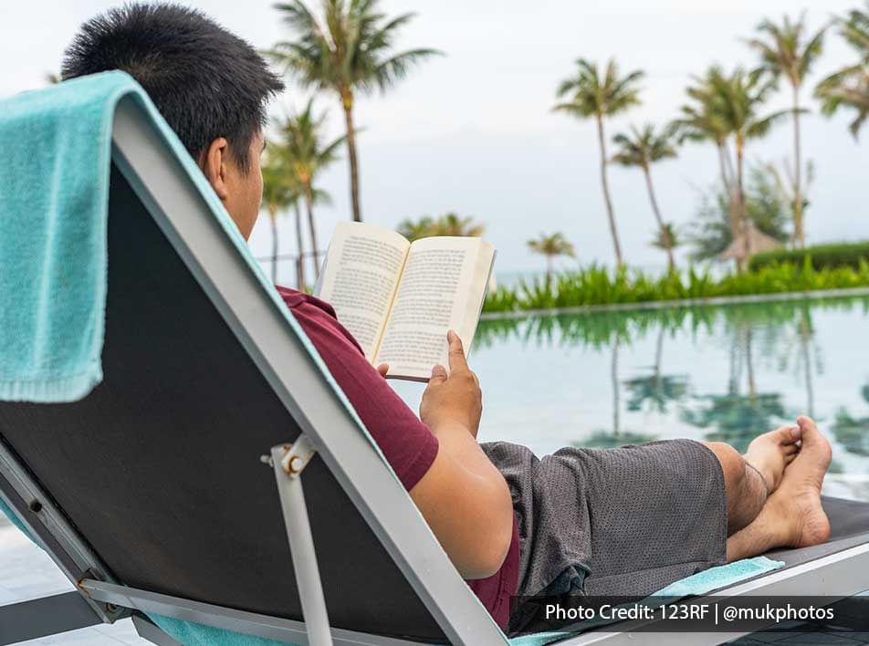 a guy reading a book while lounging on a lounge chair beside the pool - Lexis Port Dickson