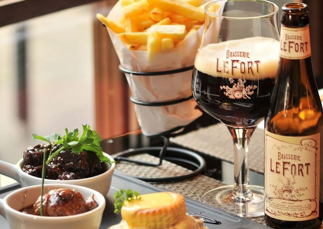 Bottled beverage and glass served with a bowl of crispy fries and savory stew at The Chutney\’s Restaurant