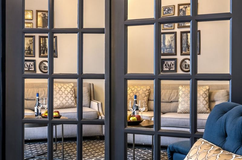 Gallery wall by a grey sofa seen through a glass-paned door in Accessible Executive Front Suite at Warwick San Francisco