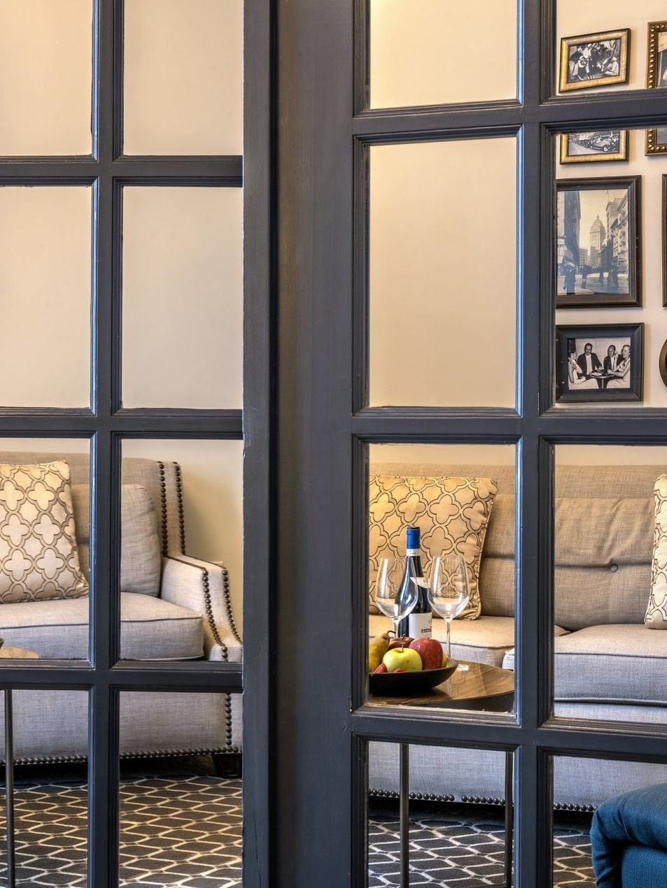 Gallery wall by a grey sofa seen through a glass-paned door in Accessible Executive Front Suite at Warwick San Francisco