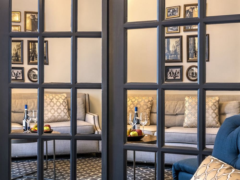 Gallery wall by a grey sofa seen through a glass-paned door in Accessible Executive Front Suite at Warwick San Francisco