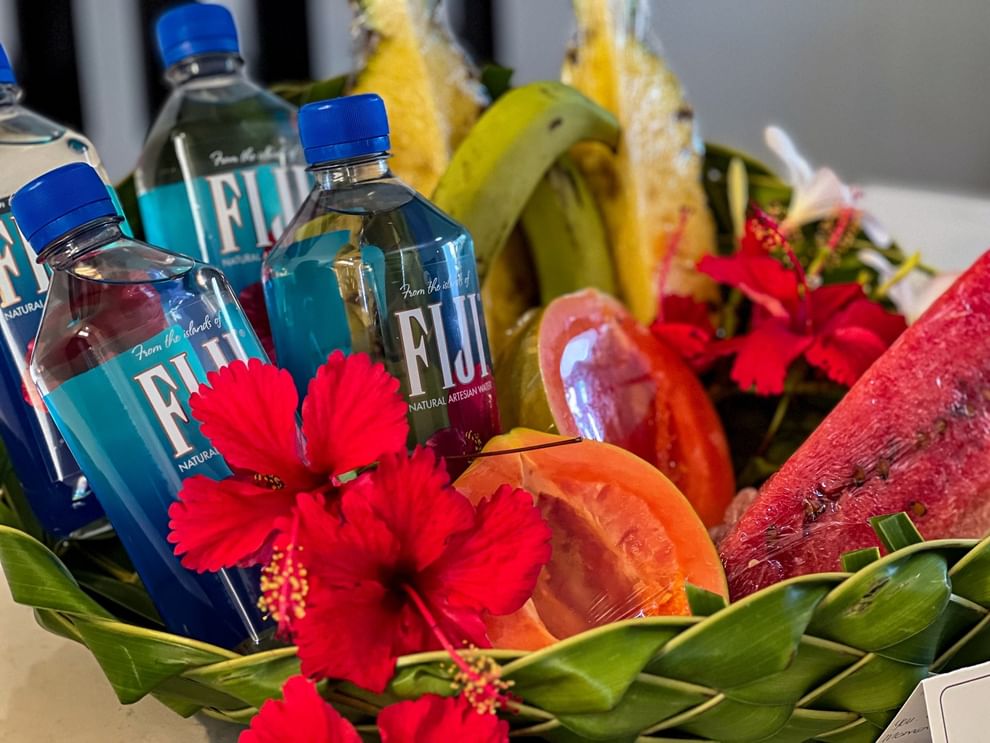 Bottles of Fiji water, fruit, and flowers in a woven basket at Tokatoka Resort - Fiji International Airport, Nadi.