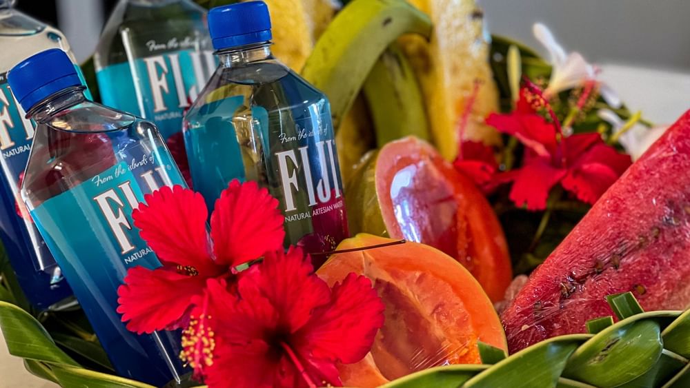 Bottles of Fiji water, fruit, and flowers in a woven basket at Tokatoka Resort - Fiji International Airport, Nadi.