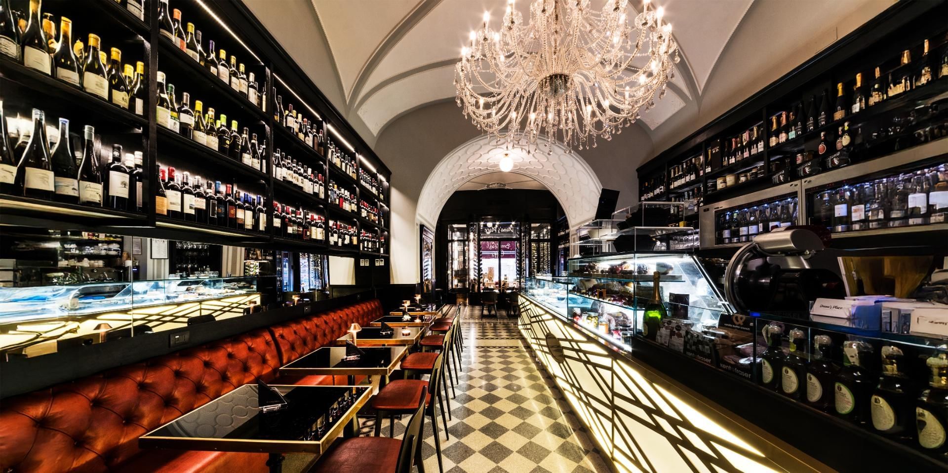 Diana's Place with a wall of wine bottles and a long leather bench under the elegant chandeliers near The Tribune Hotel