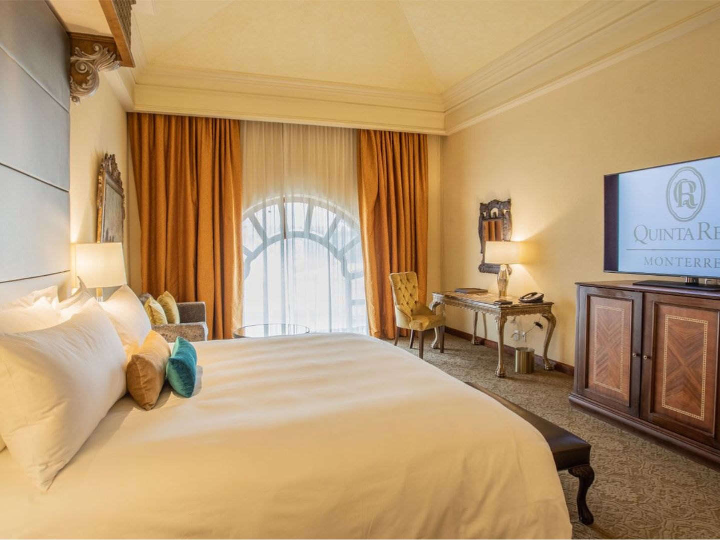 King Presidential Suite with orange curtains, a marble desk, and a large flat-screen TV at Quinta Real Monterrey