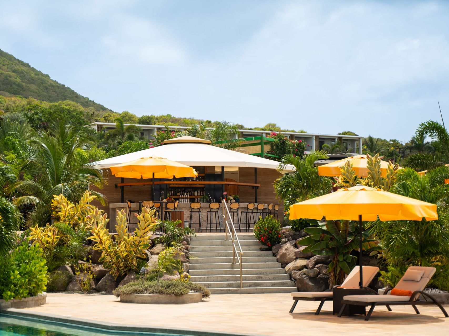 Poolbar met gele parasols, omgeven door weelderige planten, met trappen naar zitgedeelte bij Golden Rock Resort