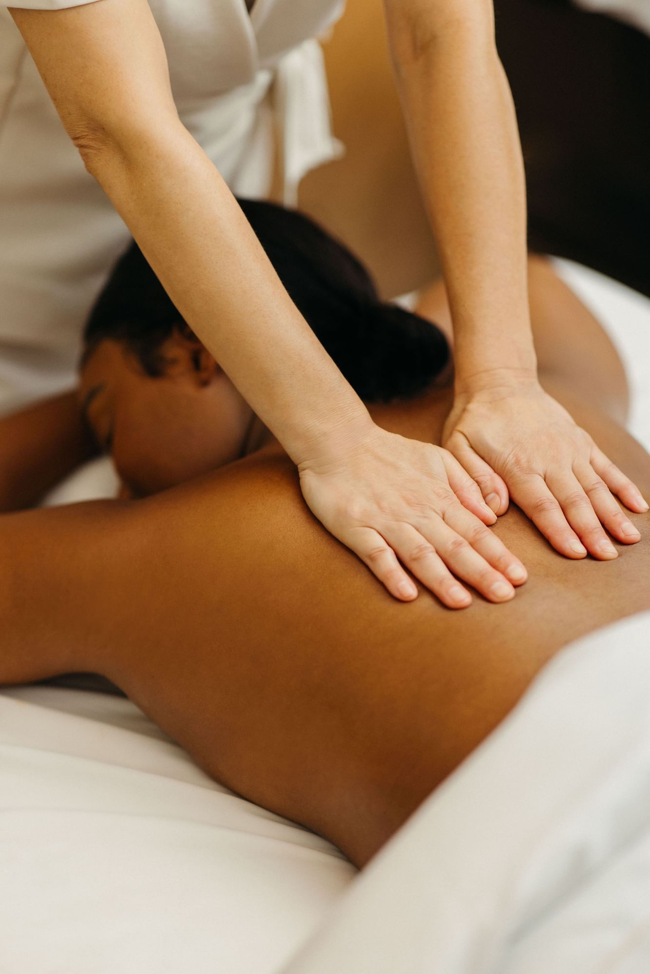 Masseuse hands giving relaxing back massage to woman lying on a plush treatment table at Guerlain Spa at Hotel X Toronto
