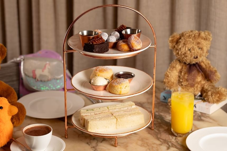 Afternoon tea setup with a tiered stand of desserts and bunnies on a table at The Kitchens