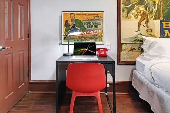 Triple Room at the Chelsea Pines Inn with desk, chair, laptop, lamp, telephone, posters, and a bed with white bedding.