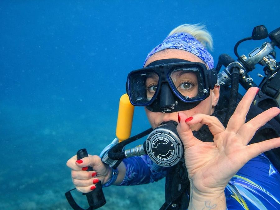 Diver underwater with snorkeling gear and scuba tank, making peace sign at Warwick Le Lagon - Vanuatu, Efate